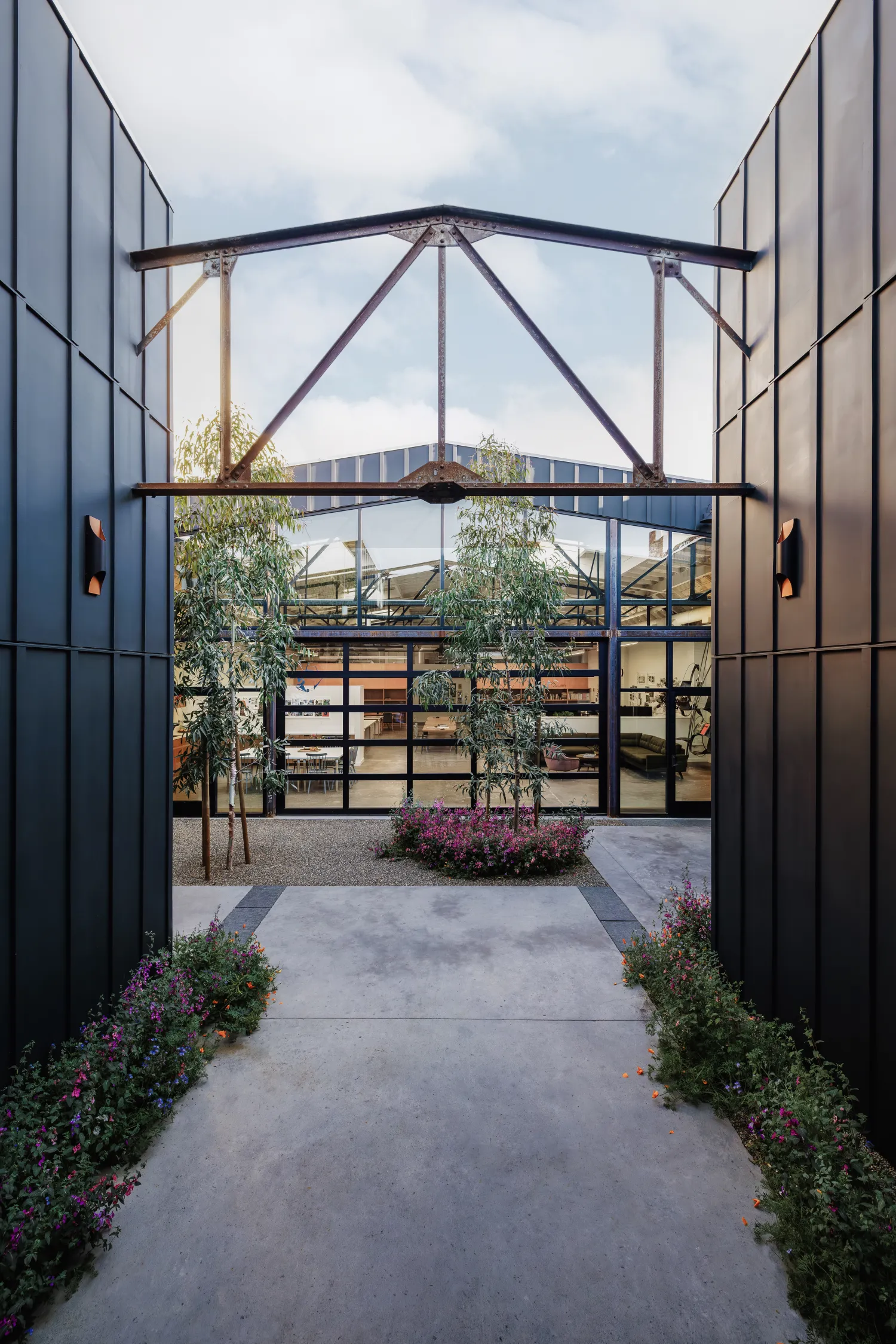 Space between two dark buildings with gravel path and view of glass and steel building 