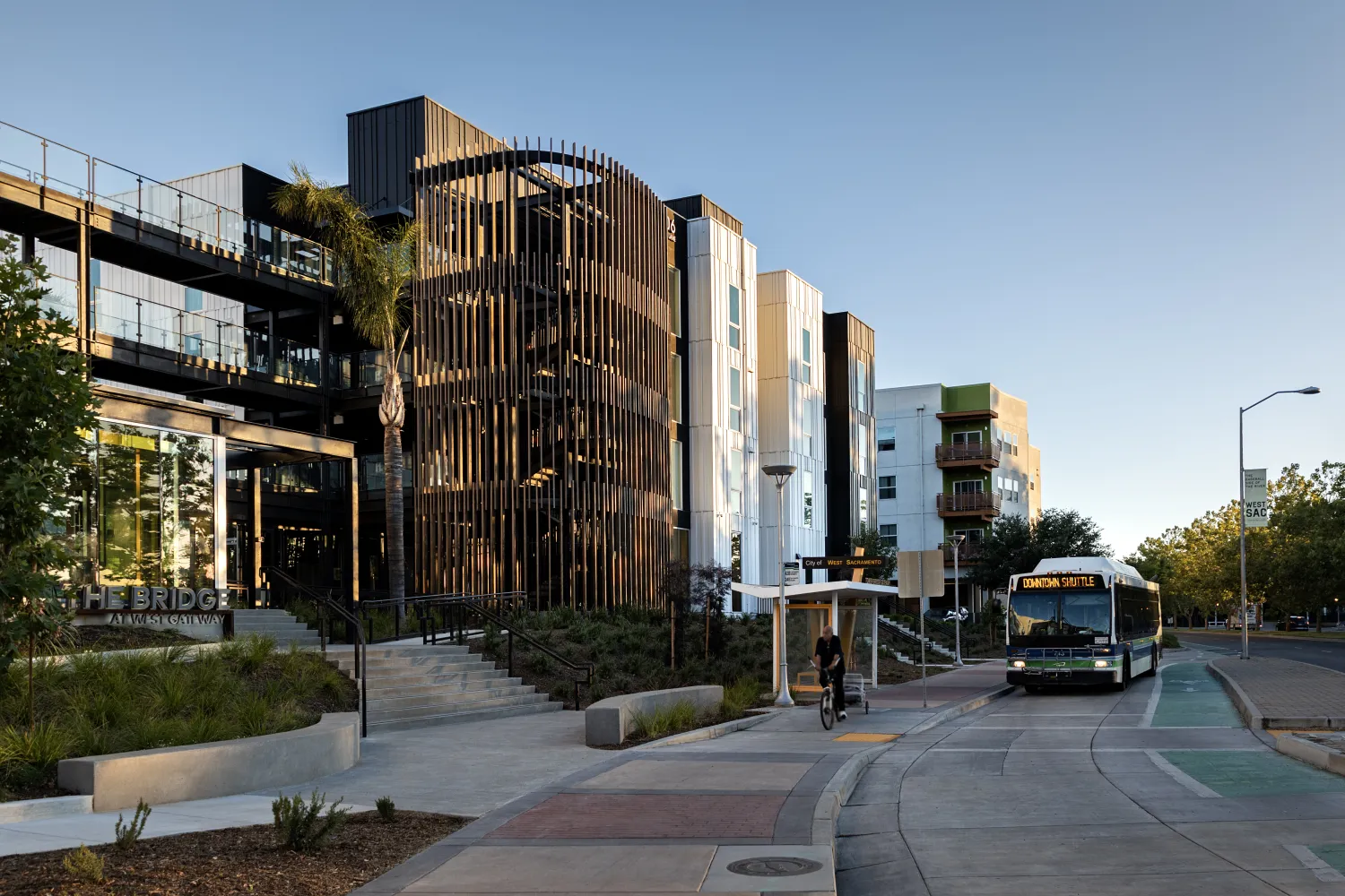Multifamily building with rounded wood-slatted stair tower, with bus at bus stop in front
