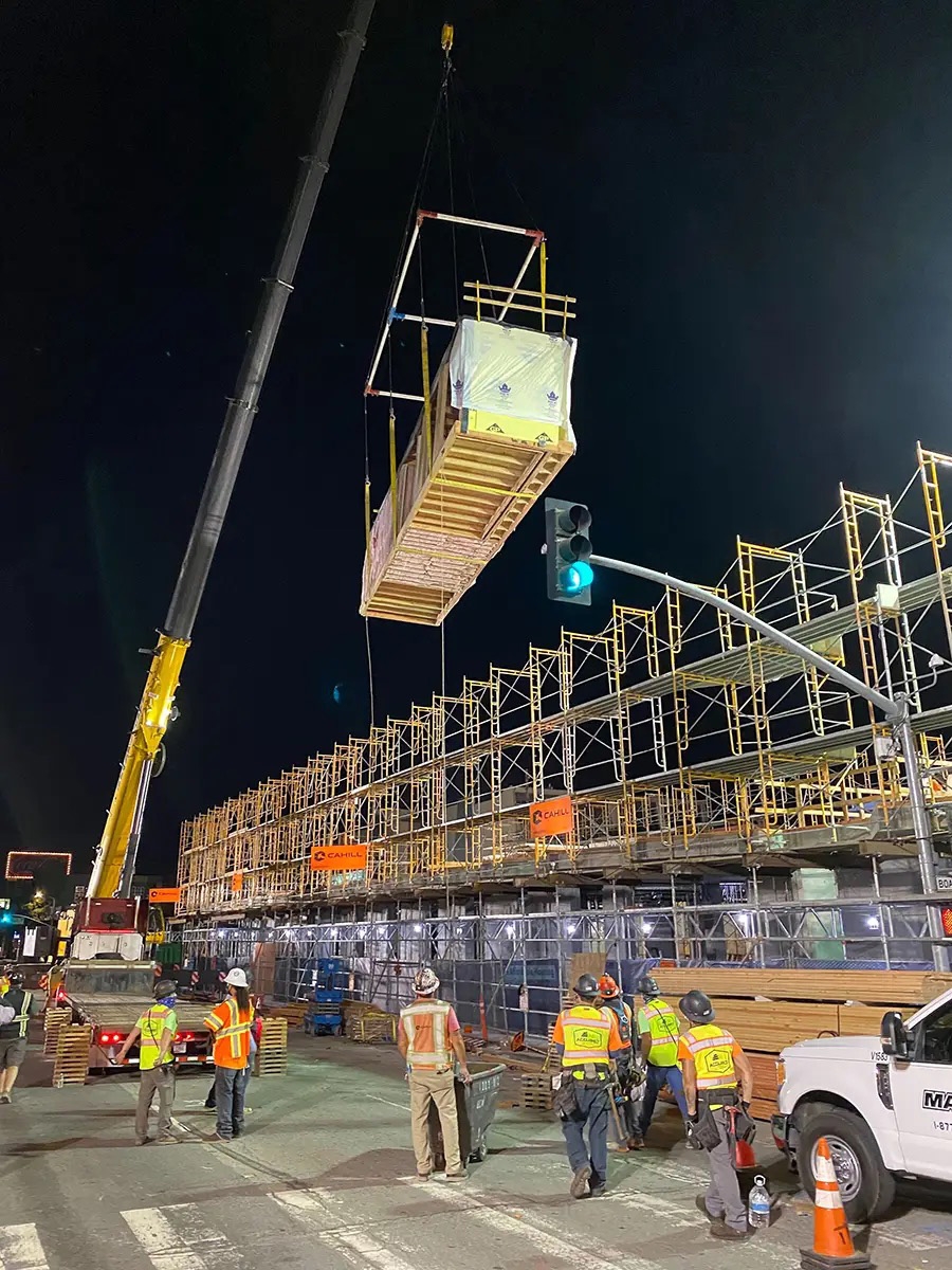 Module being craned into place on construction site at night. 