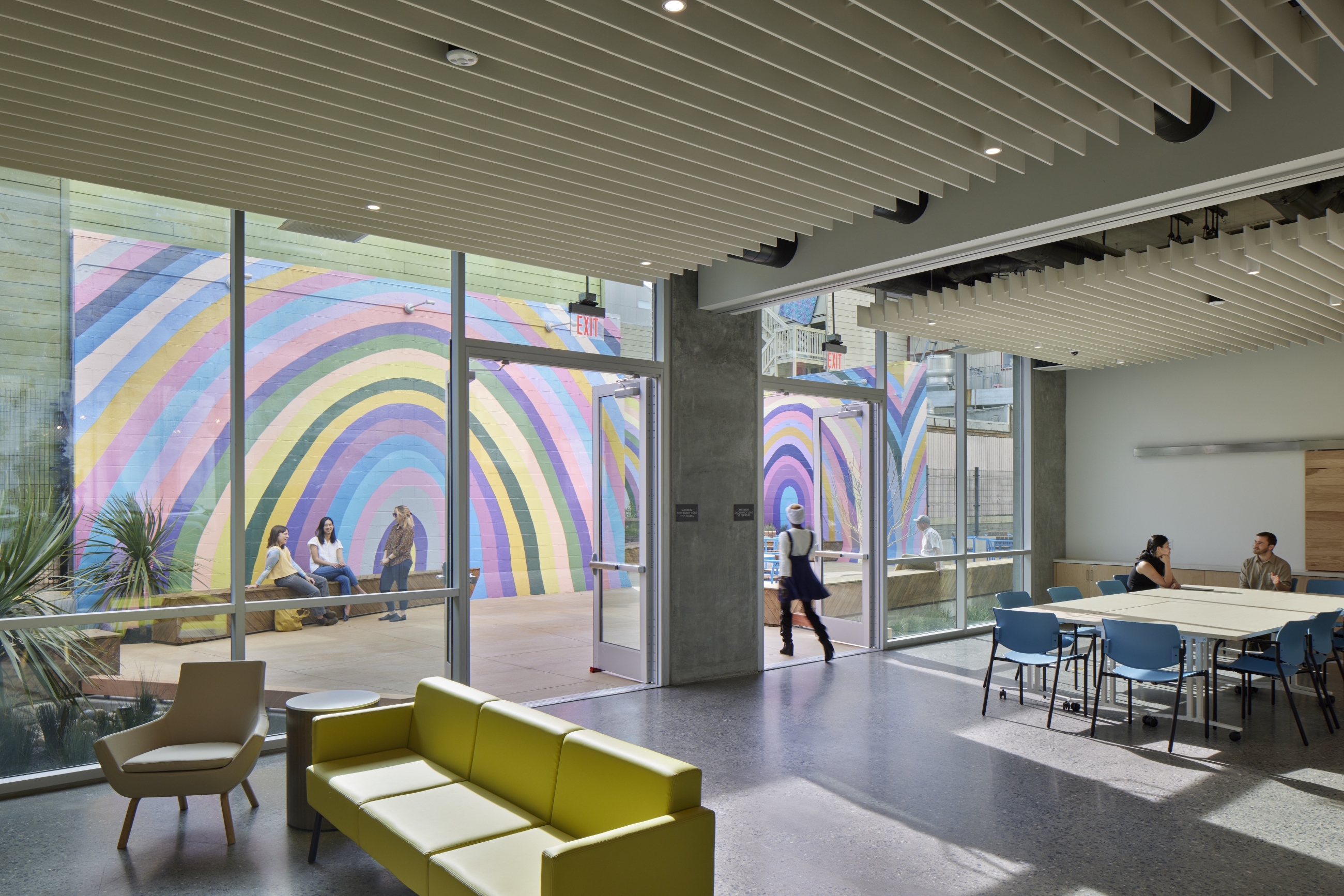 View through community room out glass wall toward courtyard, featuring rainbow murals in courtyard.