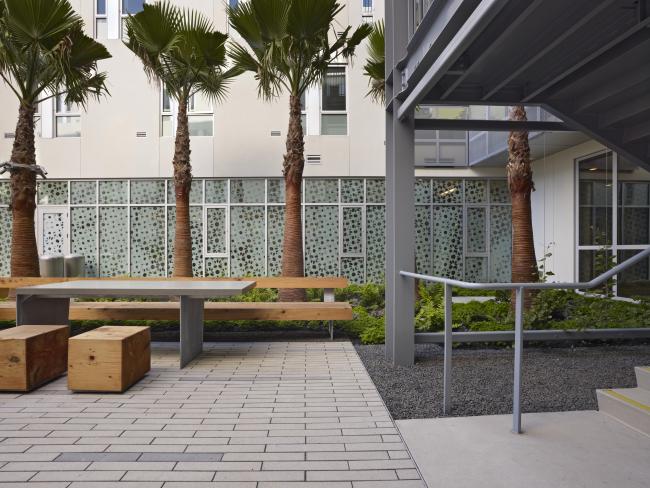 Shady detail of courtyard table and stools with privacy screen of on-site clinic