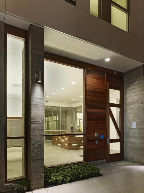 Night view of illuminated glass-front lobby and custom redwood front door at Richardson Apartments