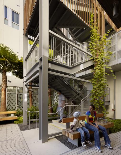 Adult and child sitting on bench at base of vine-covered open-air stair tower in Richardson courtyard