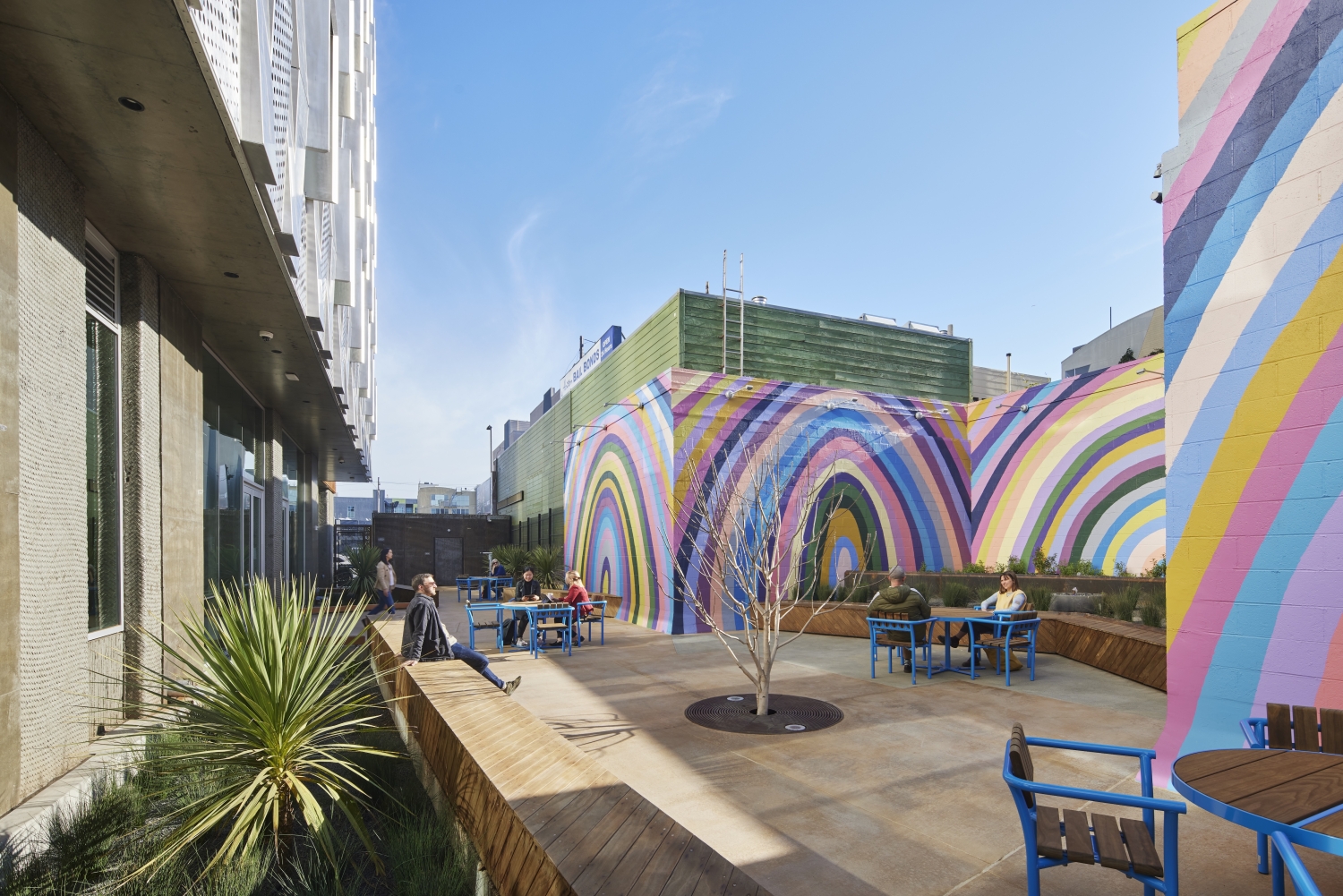 Sunny courtyard with seating, ringed by rainbow murals.