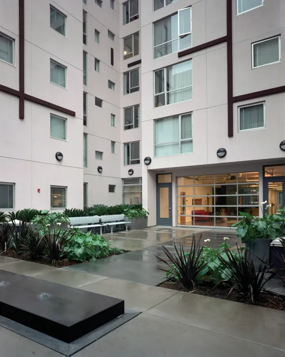 Urban courtyard with lush planting, seating, and small fountains, with concrete wet from rain.