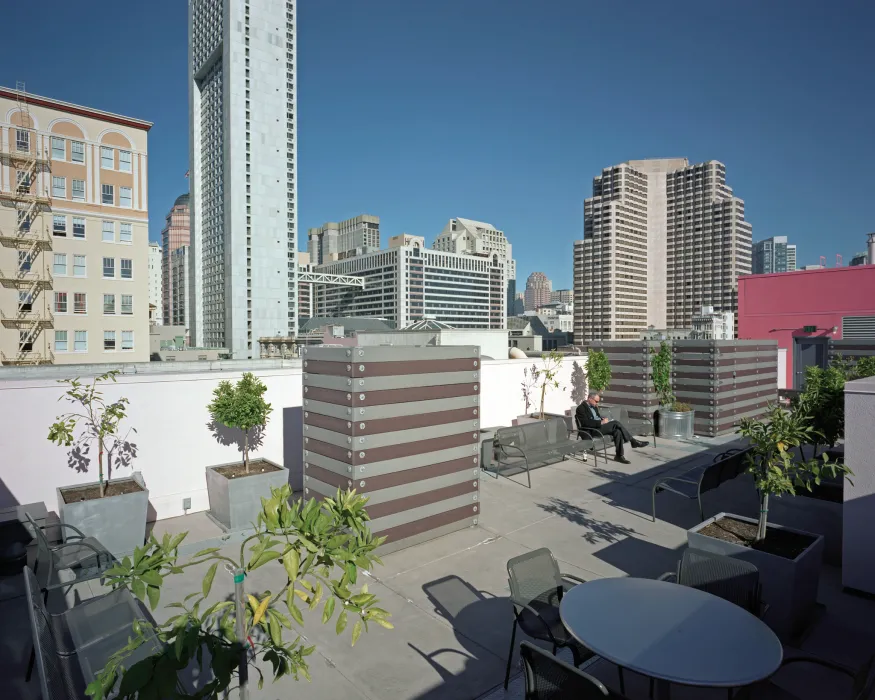 View of seating and small citrus trees in planters ringing the rooftop garden, with city views in background. 