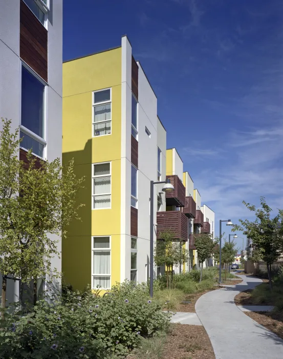 Elevation with wood-slat balconies and a planted sidewalk pathway at Tassafaronga Village in East Oakland, CA. 