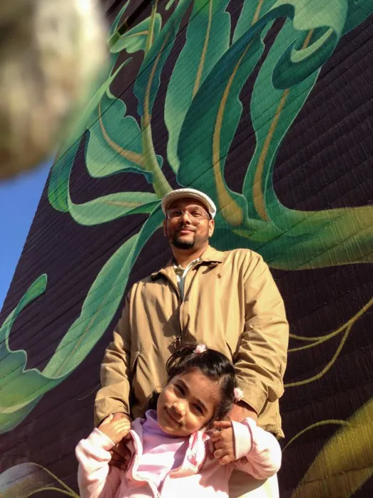 Father and daughter standing in front of the sunflower mural at Station Center Family Housing in Union City, Ca.