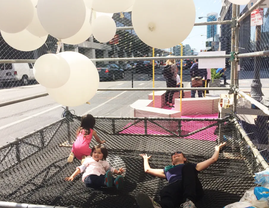 Woman and two children laying down in the net Wishing Cloud enclosure looking at the balloons.