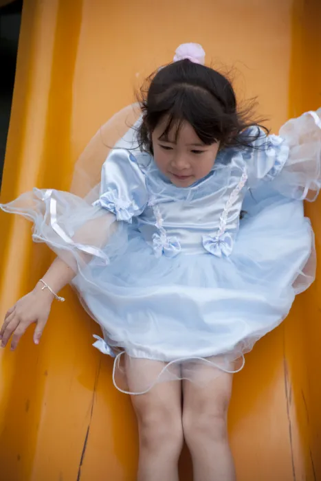 Young girl sliding down the slide in a princess costume at Paseo Senter in San Jose, California.