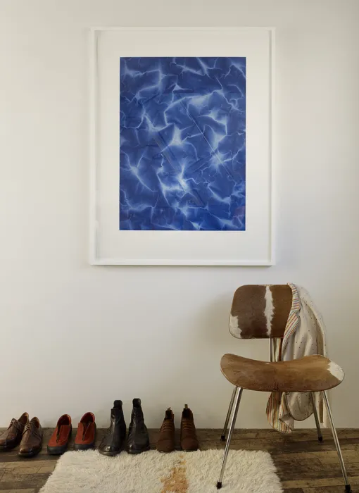 Three pairs of shoes lined up sitting next to a chair, with a blue photograph on the wall in Zero Cottage.