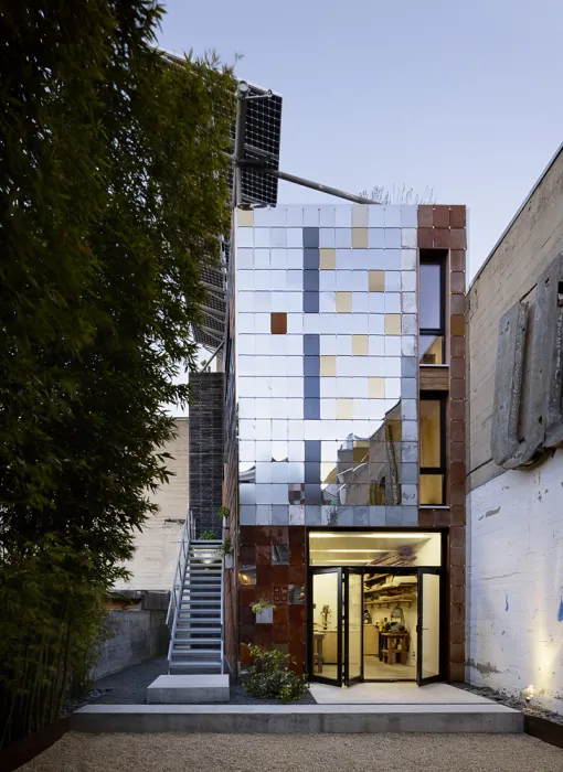 Exterior of Zero Cottage at dusk, with lights on in ground-floor workshop in San Francisco..