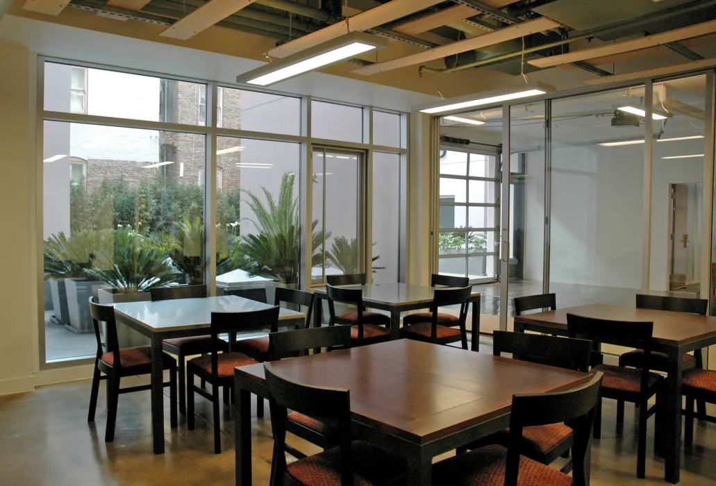 Community room with four-top tables and chairs set up for a meeting, with views out to the courtyard garden. 