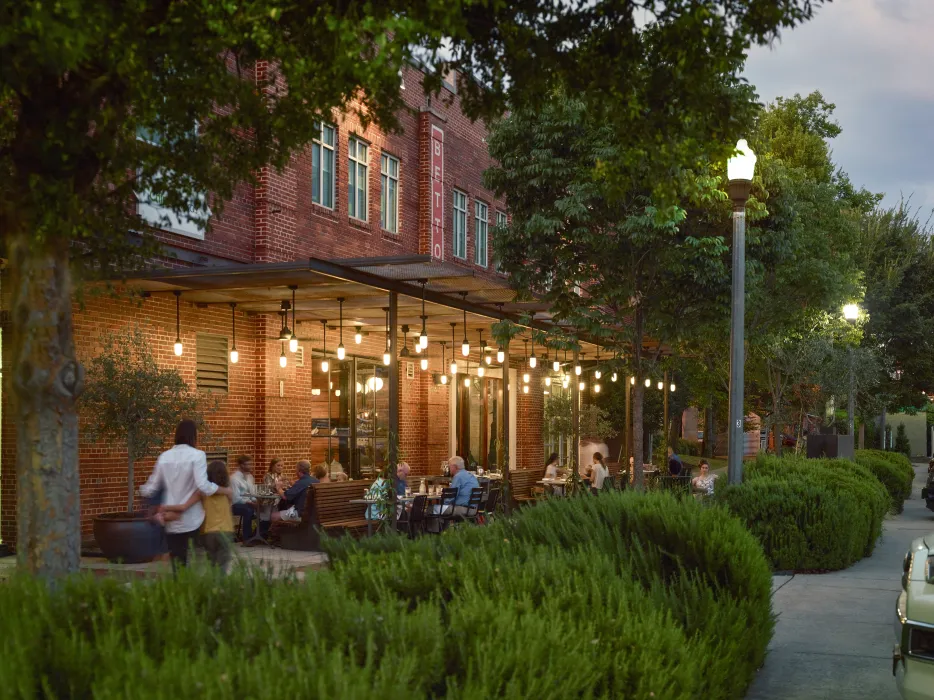 View from the southwest of people sitting at tables at Bettola Patio underneath the trellis at dusk in Birmingham, Alabama.