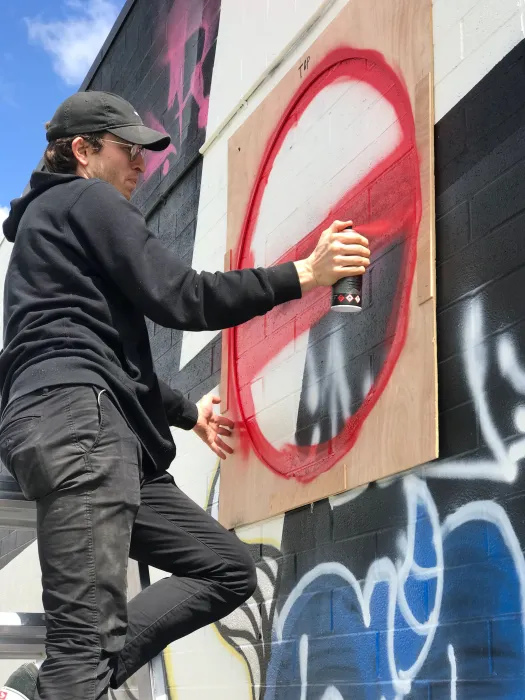 A man spray painting a red circle on the side of David Baker Architects office in Oakland, California.