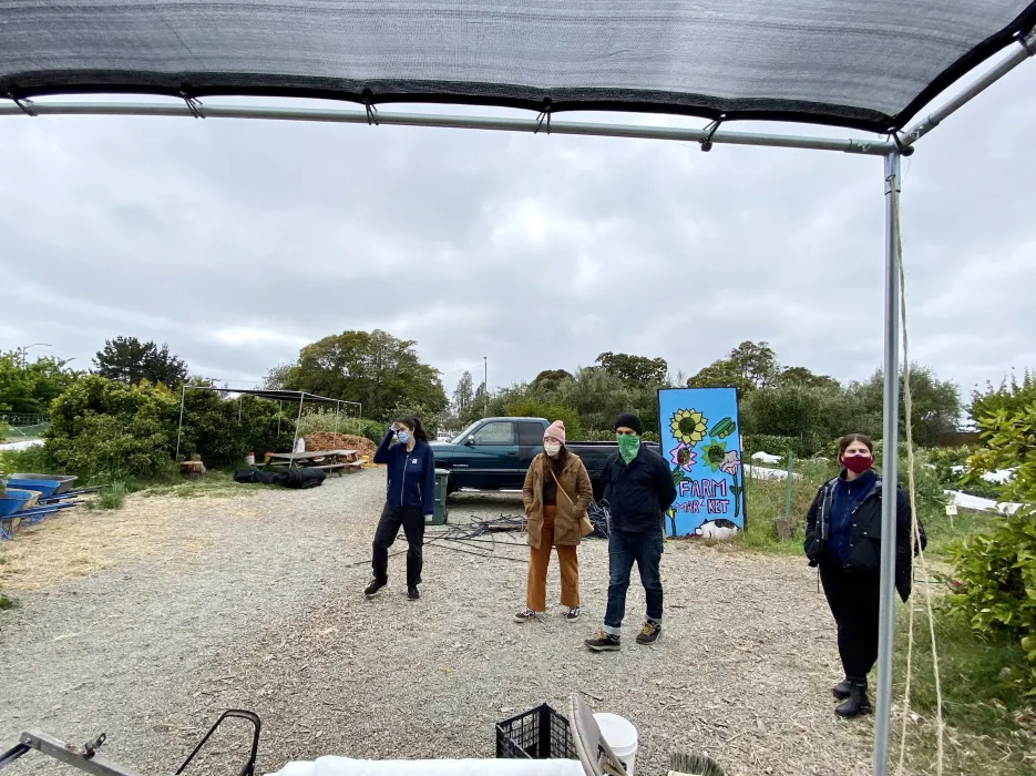 Four people standing visiting the site of the Farm2Market Shade Trellis in Alameda, California.