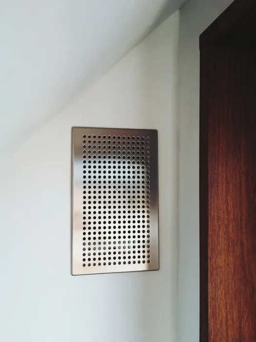 The Heat Recovery Ventilator, a silver vent on the on the wall in Zero Cottage in San Francisco.