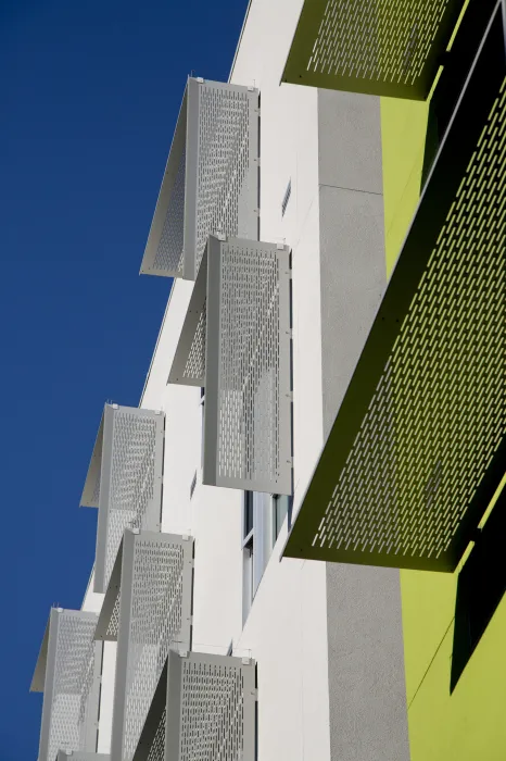 Detail of aluminum sunshades on a white and green wall at Richardson Apartments