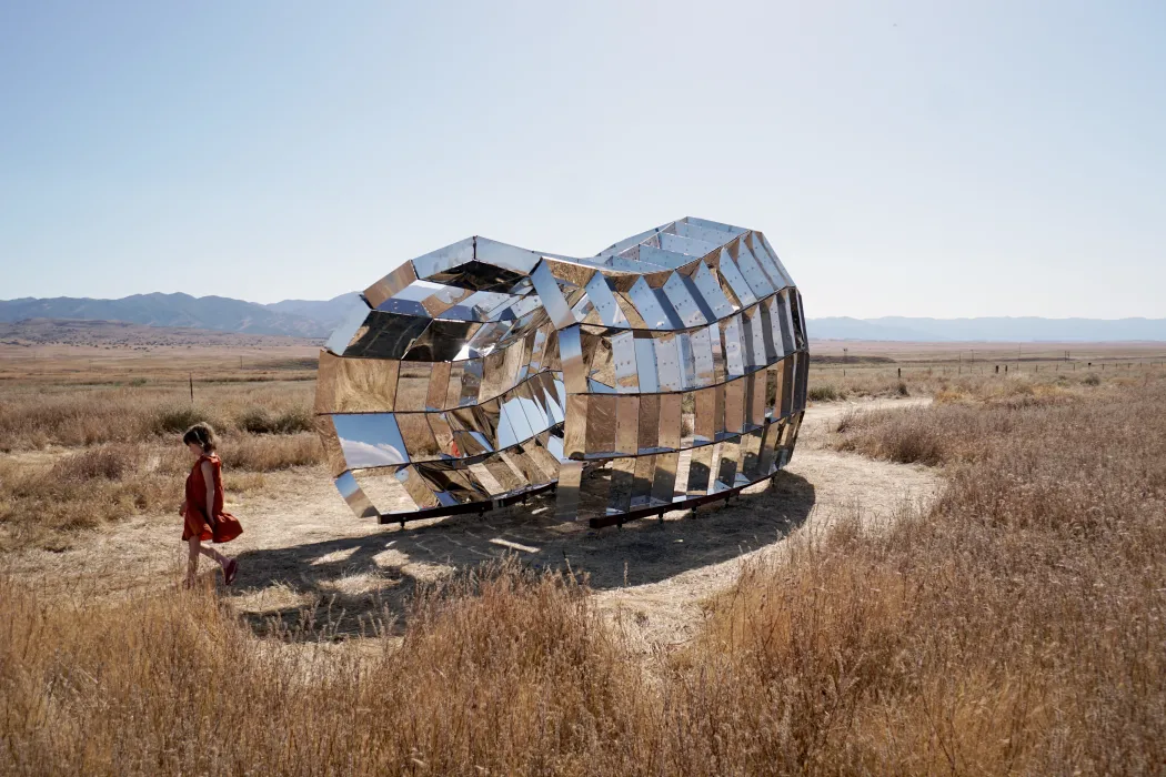 Child standing outside of peepSHOW 2.0 in the desert with mountains in the background in New Cuyama, California.