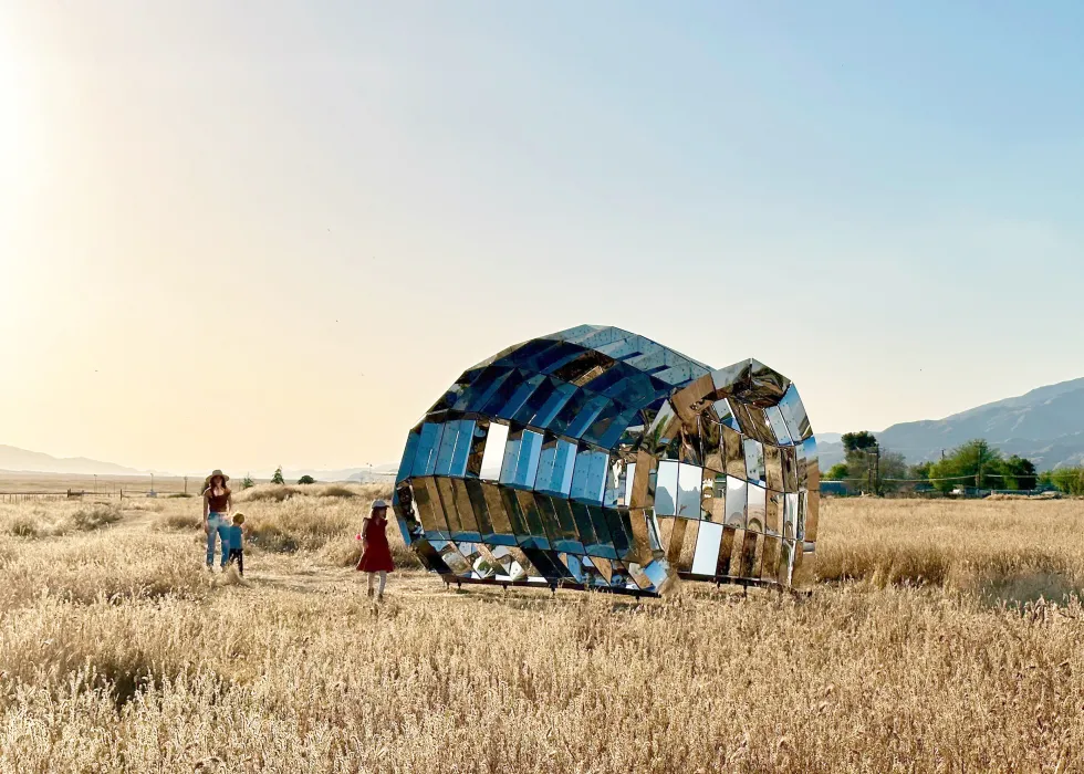 A woman and two children stand by peepshow in the desert with mountains in the background at New Cuyama, California.