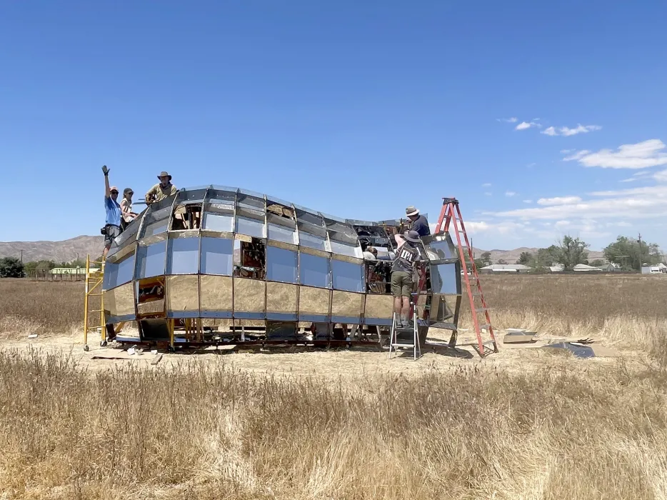 A group of people in building peepSHOW with blue skies in the desert in New Cuyama, California.