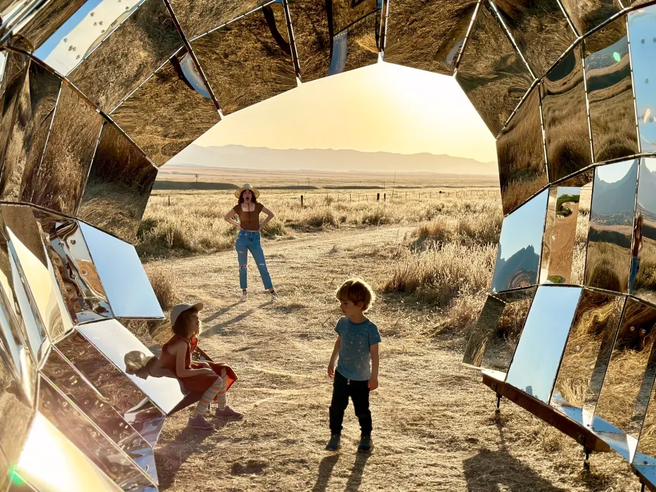 Two children playing inside the reflective peepSHOW in the sun in the desert in New Cuyama, California.