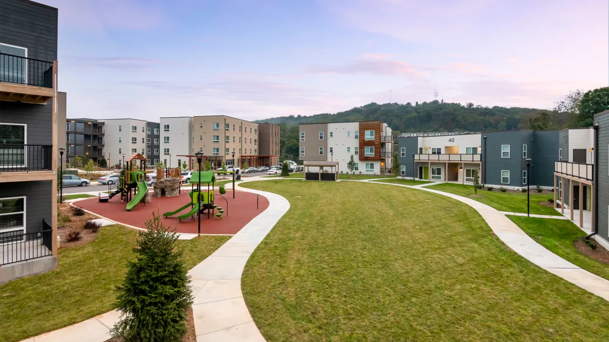 Exterior view Maple Crest Apartments surrounding a park and children's play area at at Lee Walker Heights in Asheville, North Carolina.