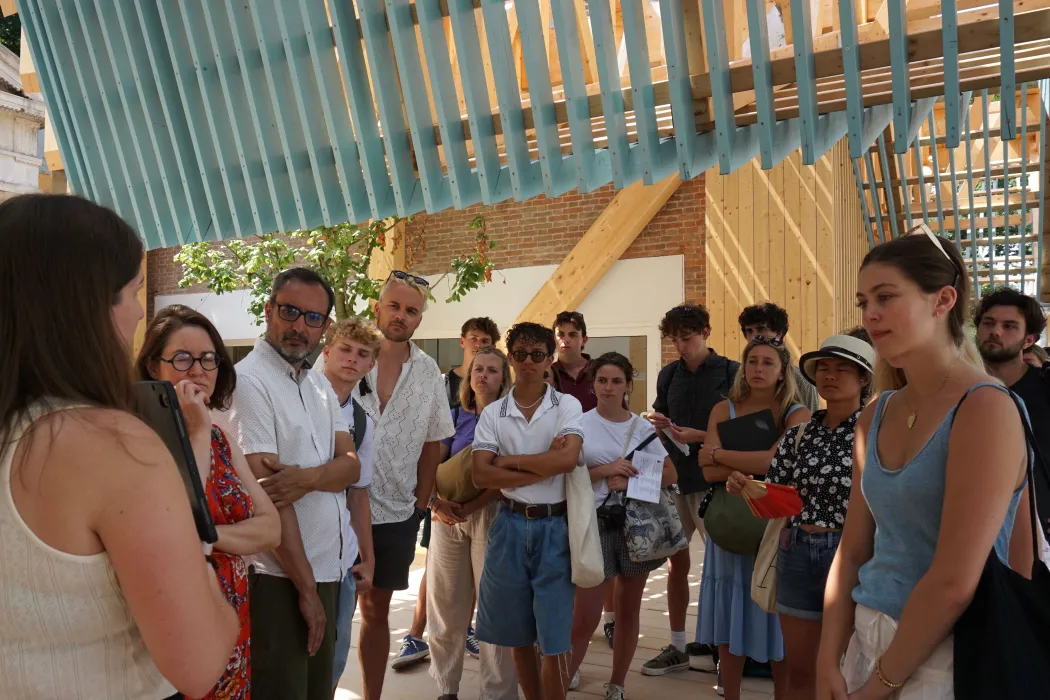 A college class gathered under the blue porch roof for a lecture