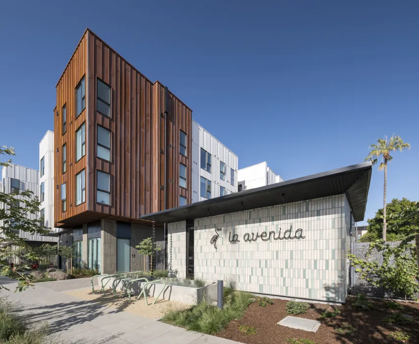 Entry of La Avenida Apartments with heron logo and building signage in cursive on a tiled wall. 
