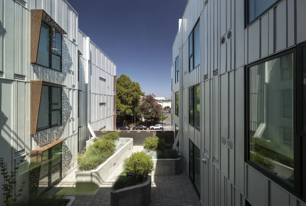 View toward street from narrow podium courtyard with planter boxes and perforated sunshades. 
