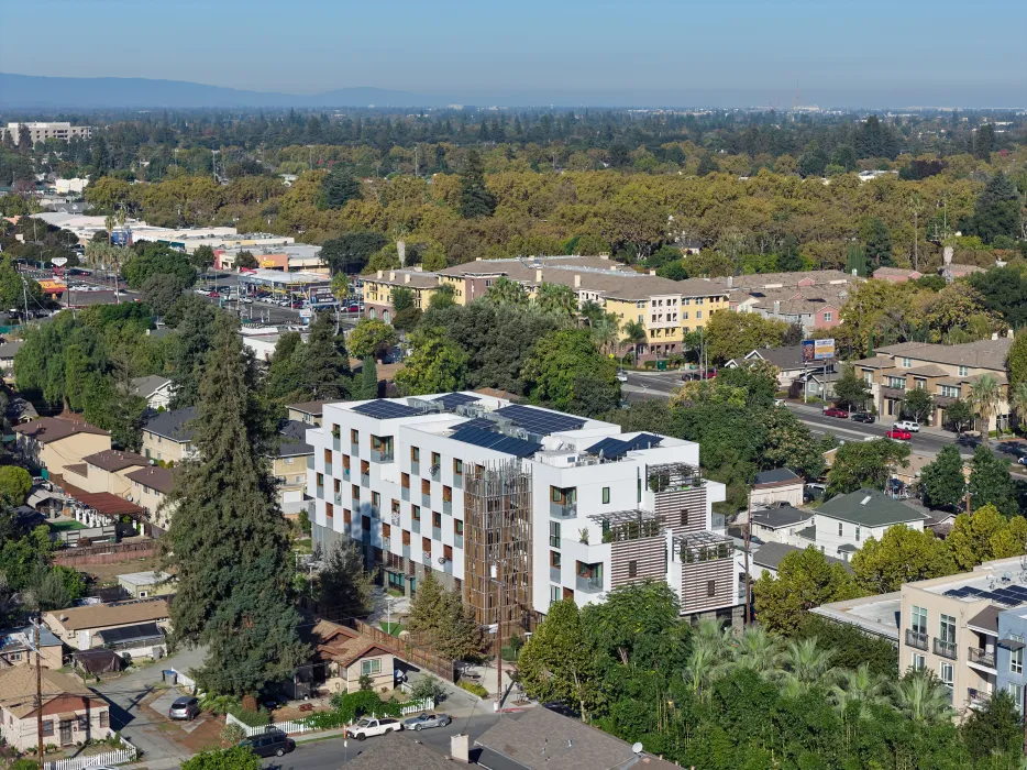 Aerial view of front corner of white apartment building in cityscape with hills and blue sky in background