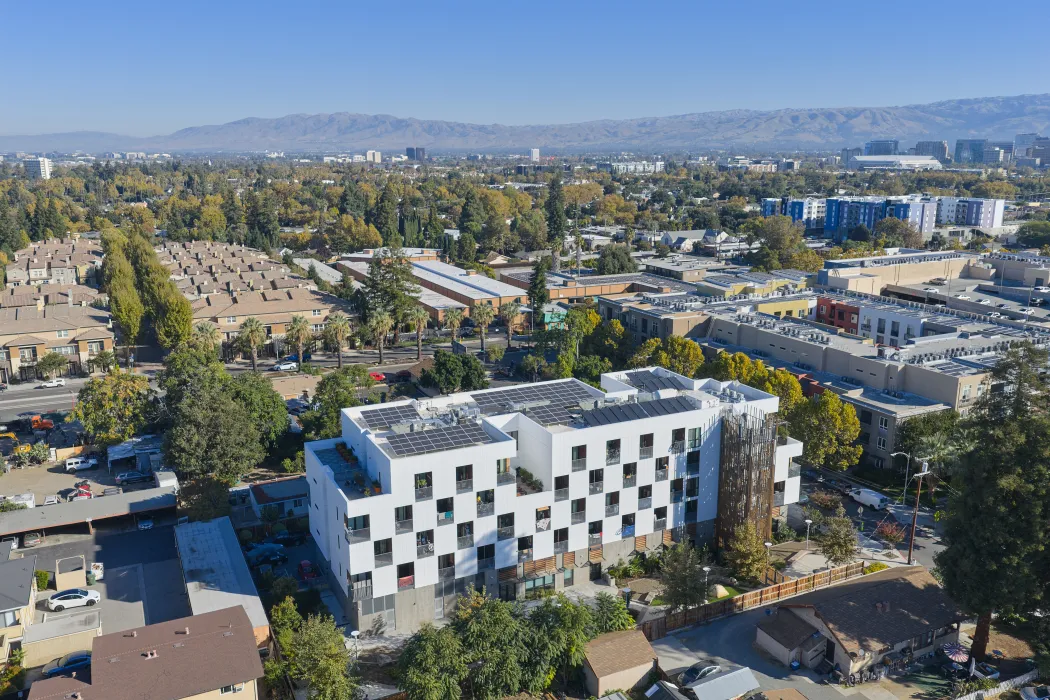 Aerial view of side of white apartment building in cityscape with hills and blue sky in background
