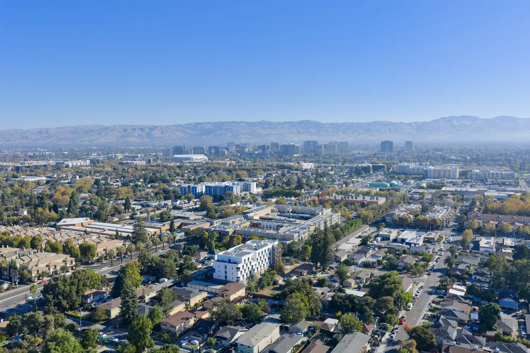 Distant aerial view of white apartment building in cityscape with hills and blue sky in background