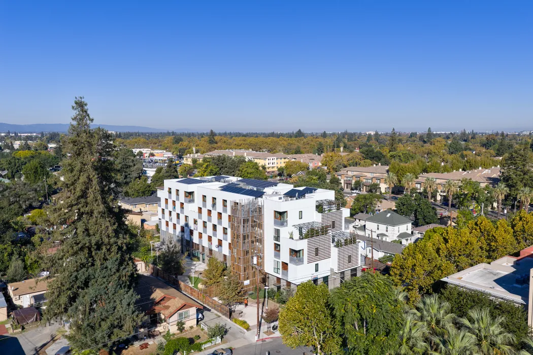 Aerial view of front corner of white apartment building in cityscape with hills and blue sky in background
