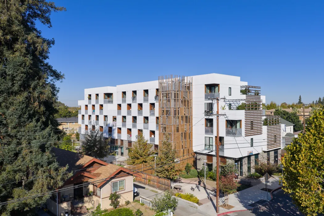 White apartment building with decorative wood stair tower and balconies in a checkerboard pattern