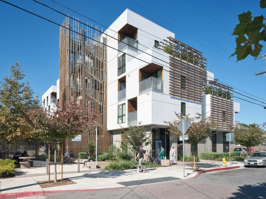 Corner view of white apartment building with wooden stair tower, trellises, and blue front door