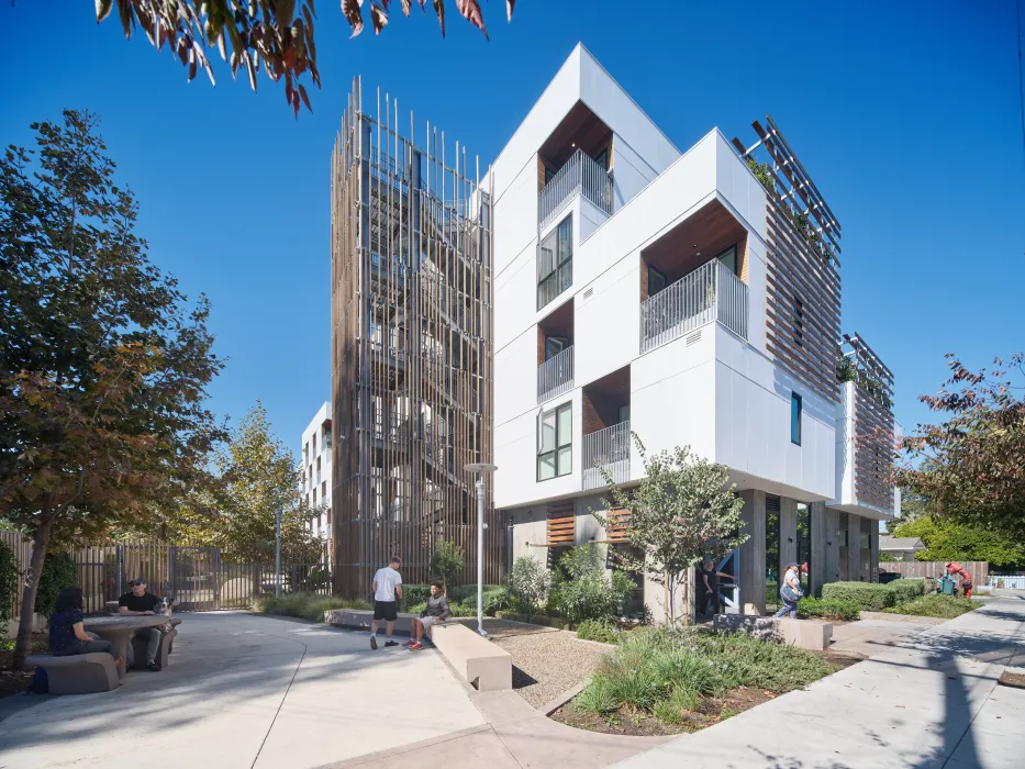 Corner view and entry plaza of white apartment building with wood stair tower