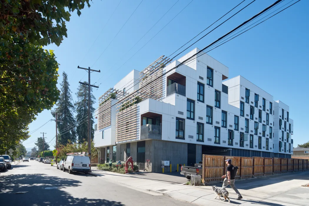 Corner view of white apartment building with wood trellises and driveway entry