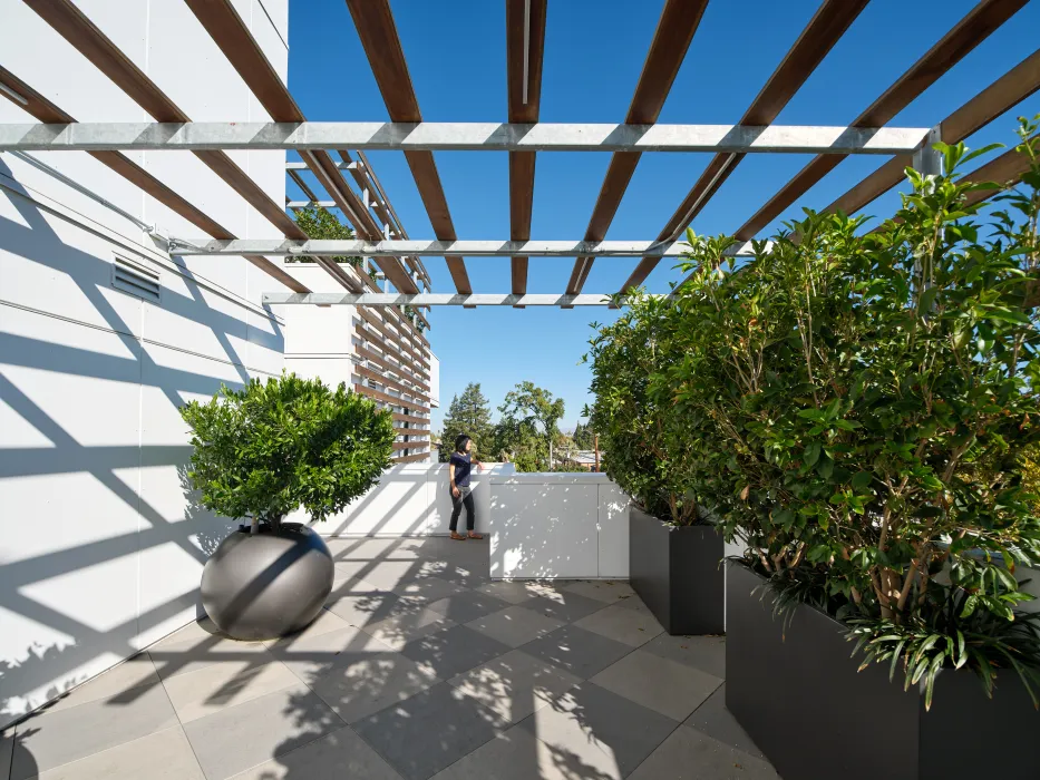 Patio view with planters, overhead trellis, and woman looking out at view