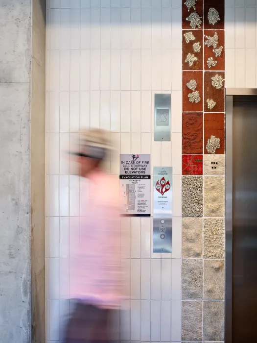 Detail view of white tile wall with textured tile inset and blurry figure waliking past