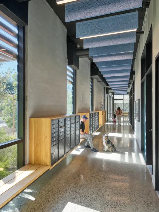 Interior lobby hallway with apartment mailboxes, a man sitting on a bench with a dog, and a woman and child walking in the distance