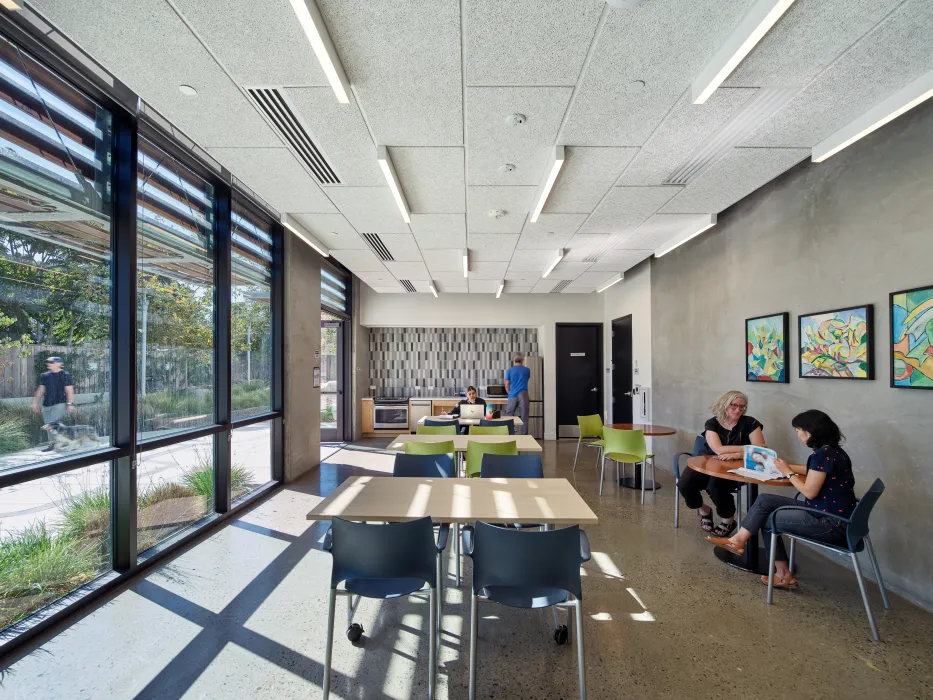 Interior of community room with glass wall at left and people sitting and reading