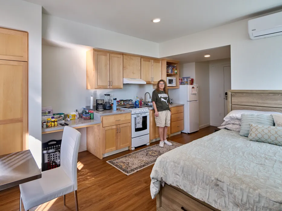 Interior view of studio apartment with woman in green T shirt and shorts posing by the stove