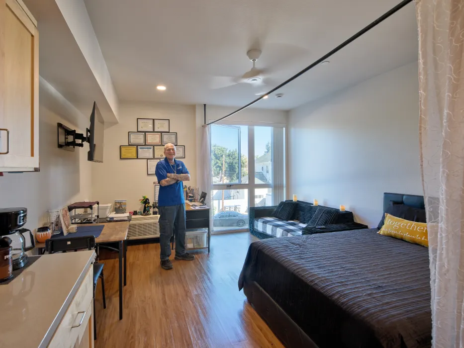 Interior view of studio apartment with man in blue standing with folded arms
