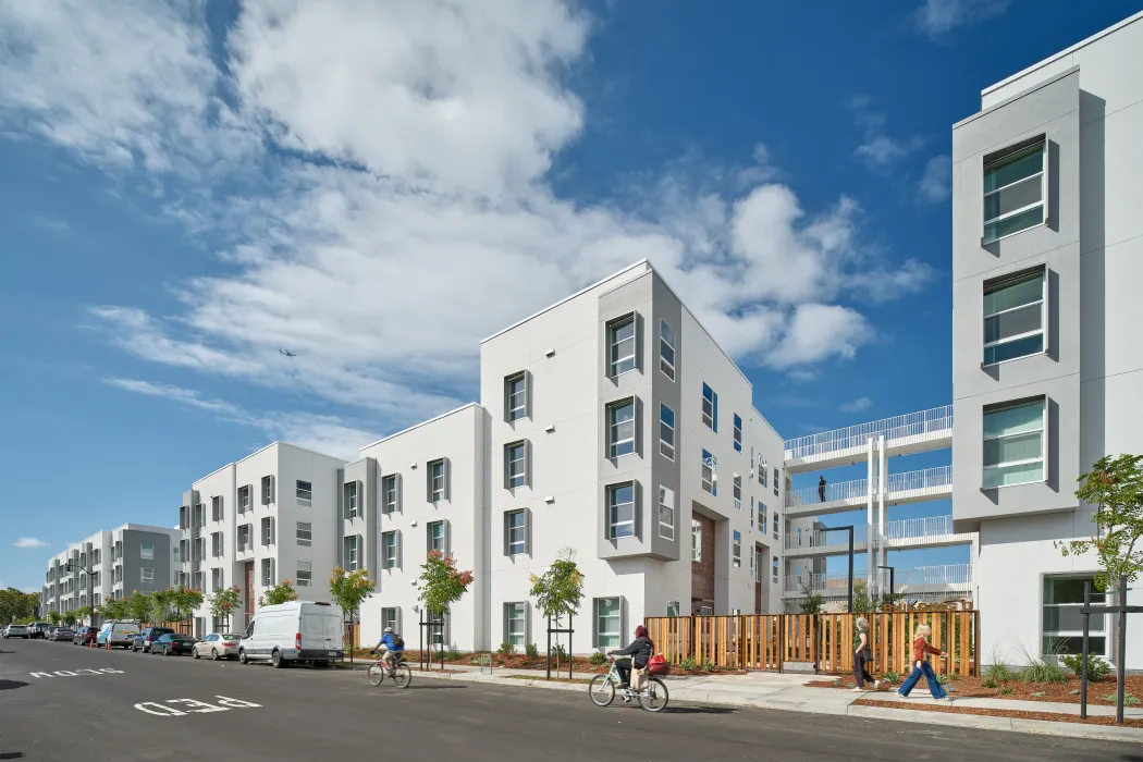 Large white building with gray bays, sunshades, and open-air circulation against blue sky