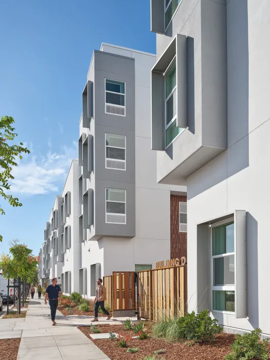 View down sidewalk showing wooden fence and gate in white and gray building