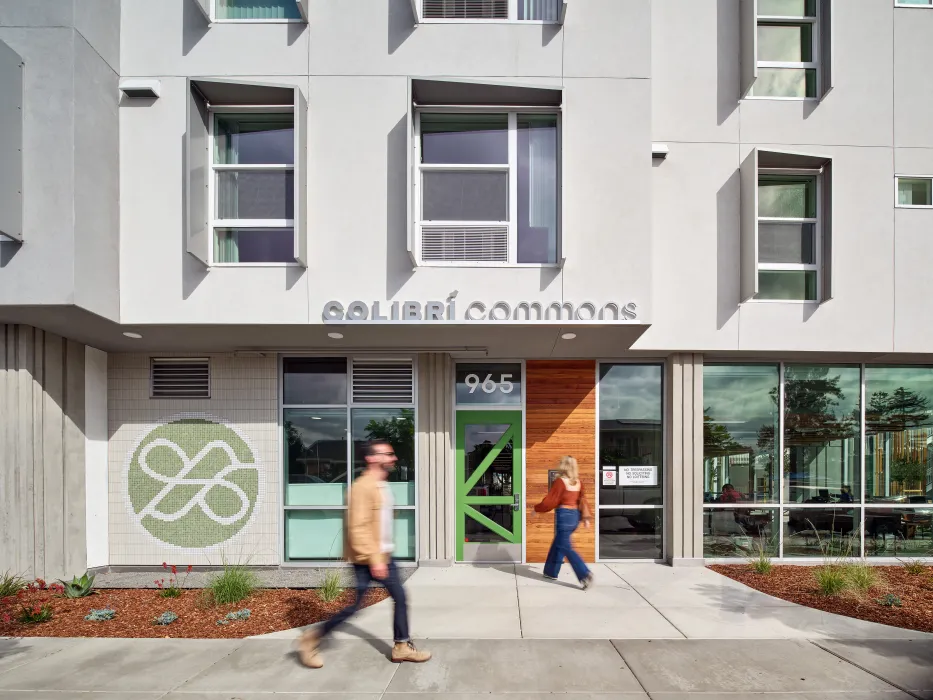 Entry plaza of white building with green hummingbird mural and bright green front door