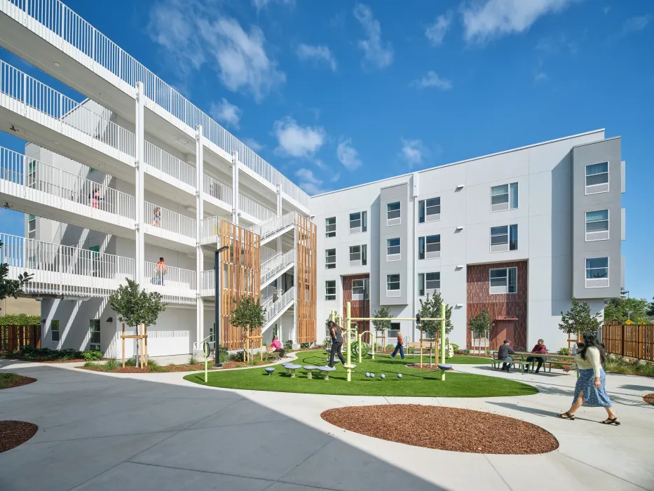 Angled view of courtyard play area, wood stair towrer, and open-air hallways in large white building