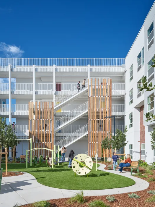 View of courtyard play structure and wood-lined stair tower of large white building against bright blue skyains
