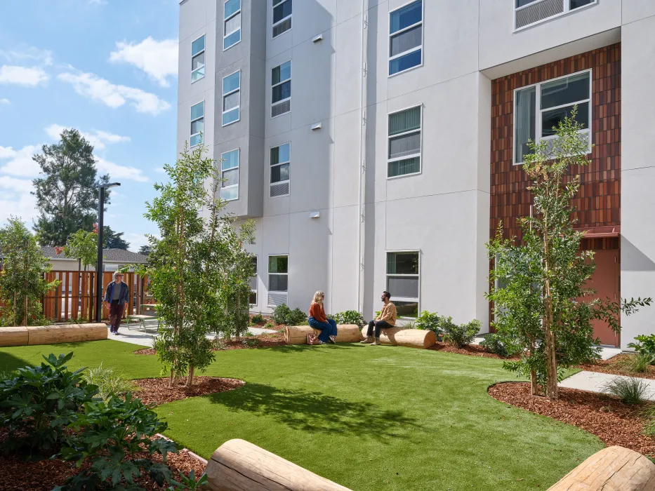 Small courtyard with grass and people sitting on benches fashioned from whole logs